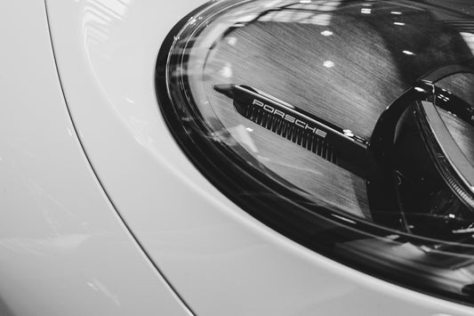 Close-up of a white car's headlight with porsche logo.