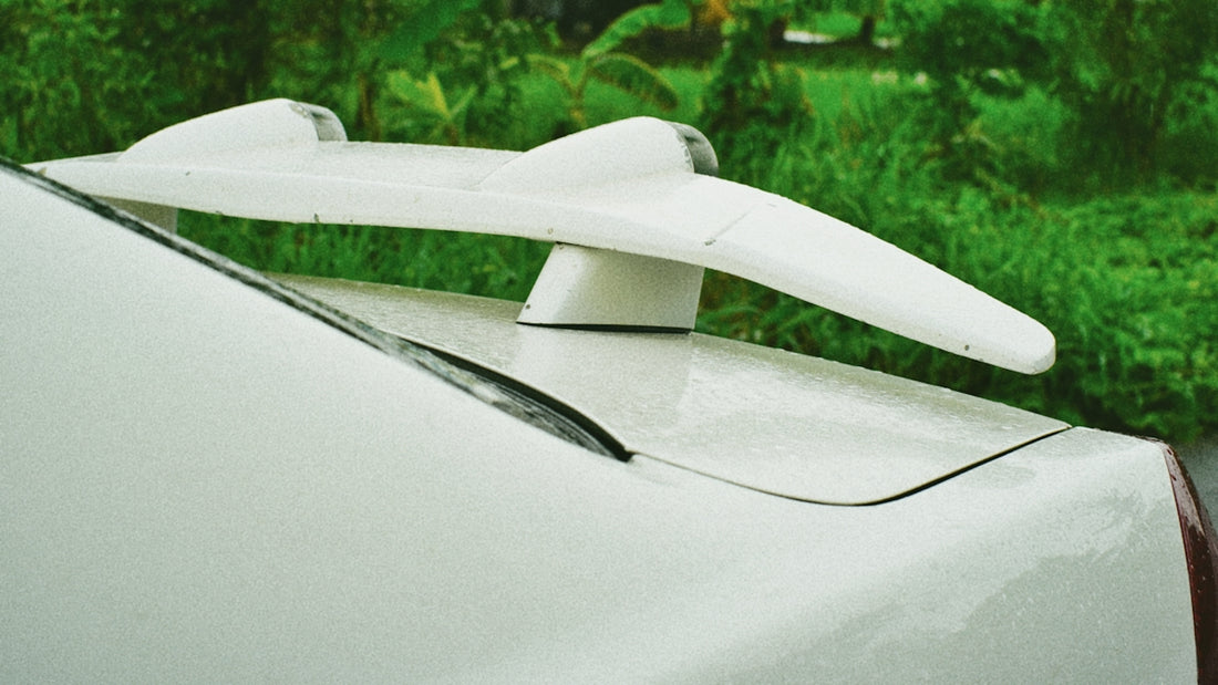 White car with a prominent white spoiler against green foliage.